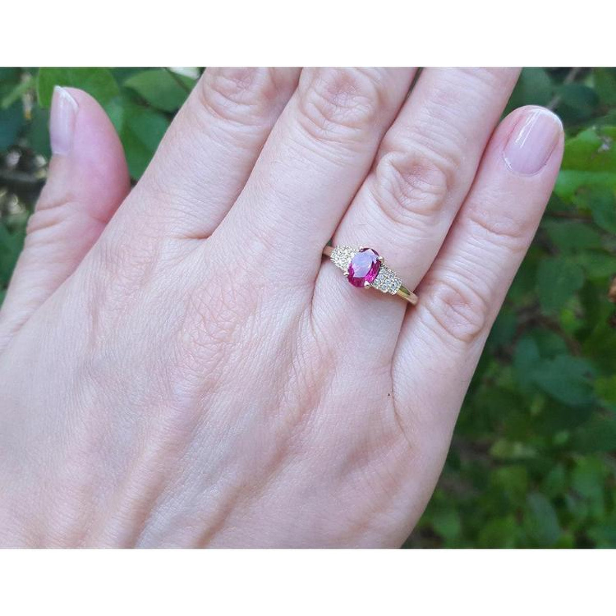 Genuine oval cut Burmese ruby ring with side diamonds set in 14k yellow gold on a woman's finger.