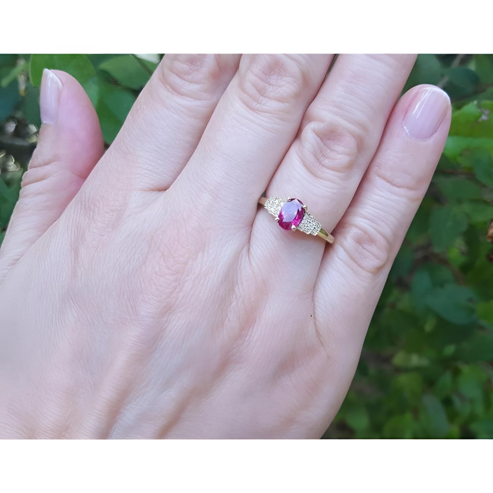Genuine oval cut Burmese ruby ring with side diamonds set in 14k yellow gold on a woman's finger.