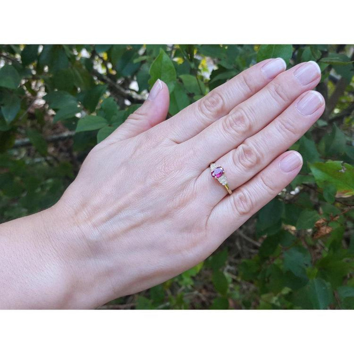Woman's hand wearing a 14k yellow gold ring with a deep red oval ruby and side diamonds.