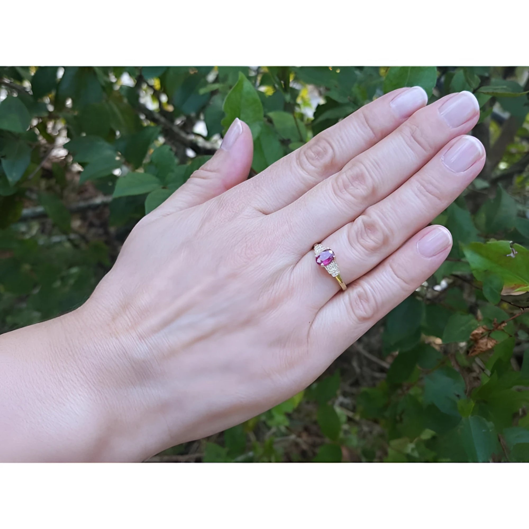 Woman's hand wearing a 14k yellow gold ring with a deep red oval ruby and side diamonds.