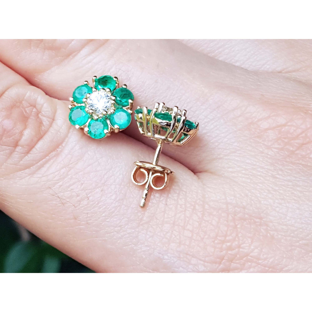 Pair of emerald and diamond earrings on a hand