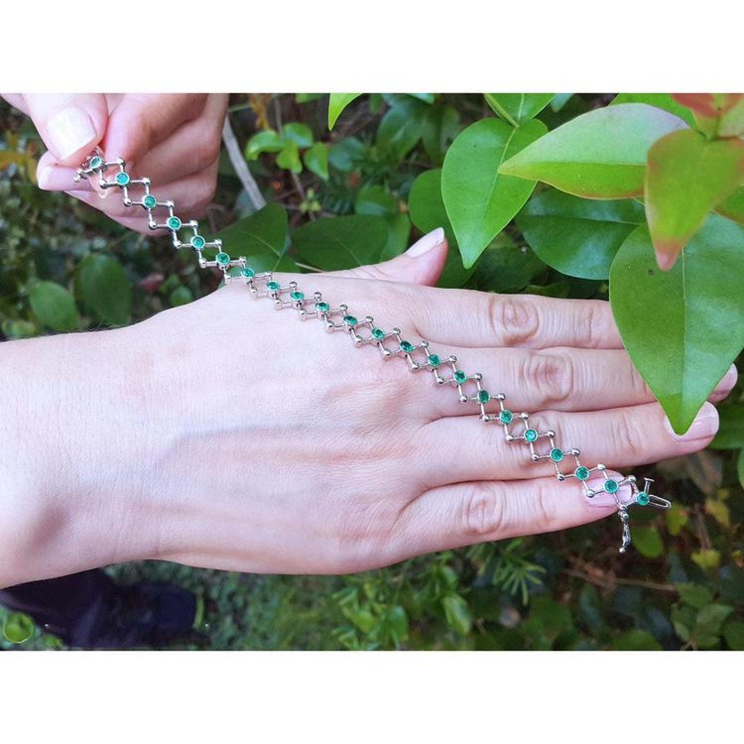 14K white gold bracelet with round Colombian emeralds in bezel-set, diamond-shaped links on a woman's hand.