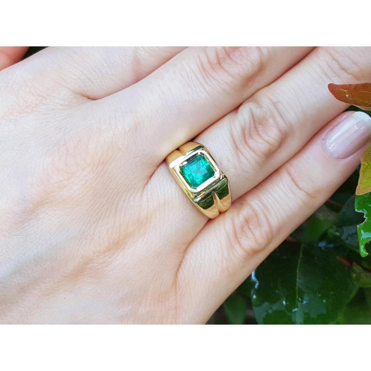 A yellow gold emerald ring bezel set on a hand, with a natural background