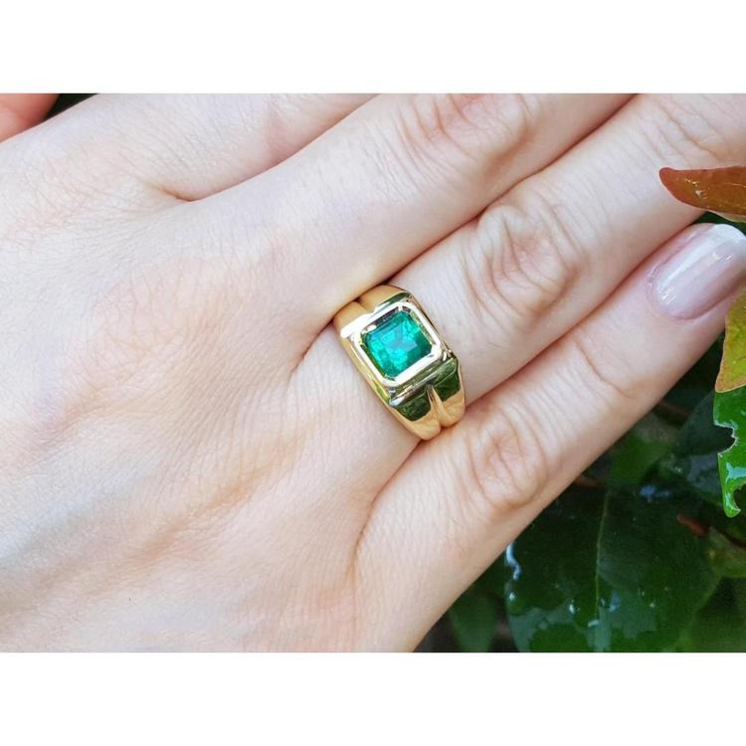 1.53 ct. square emerald solitaire ring in a yellow gold bezel setting on a hand.