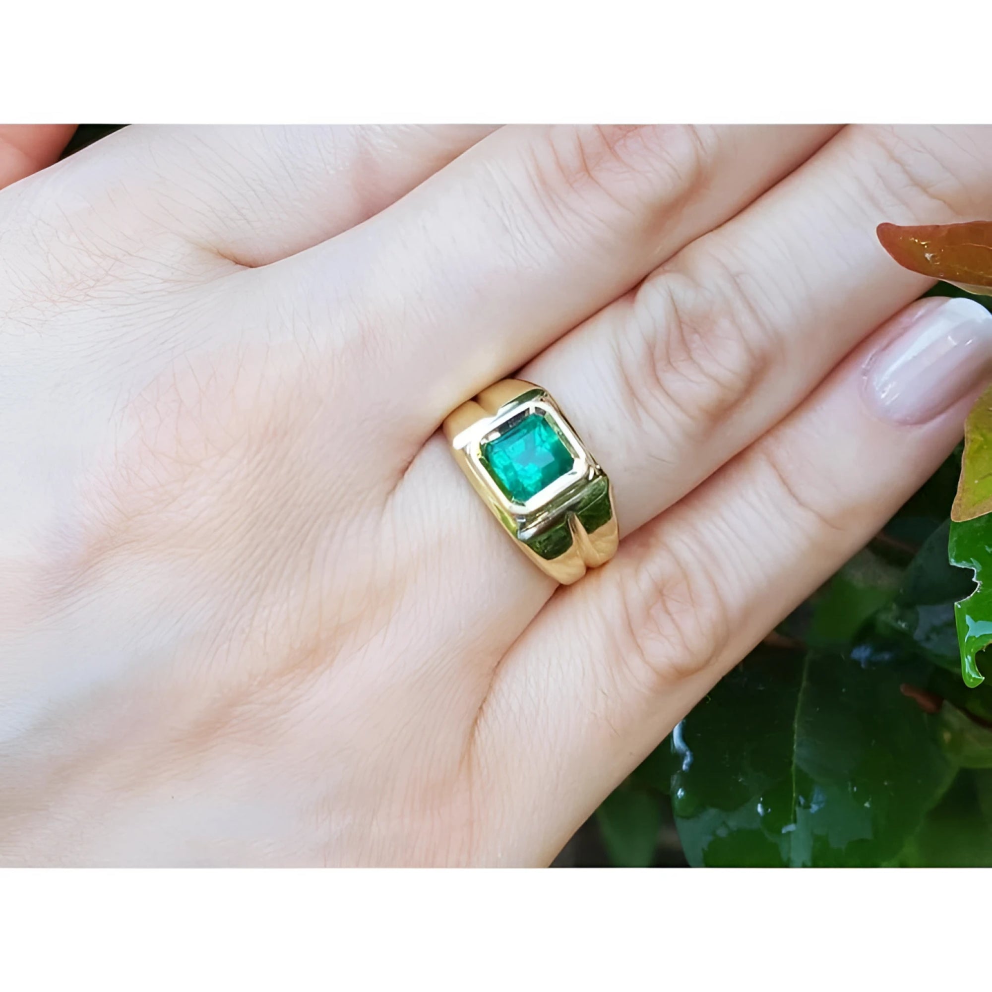 1.53 ct. square emerald solitaire ring in a yellow gold bezel setting on a hand.