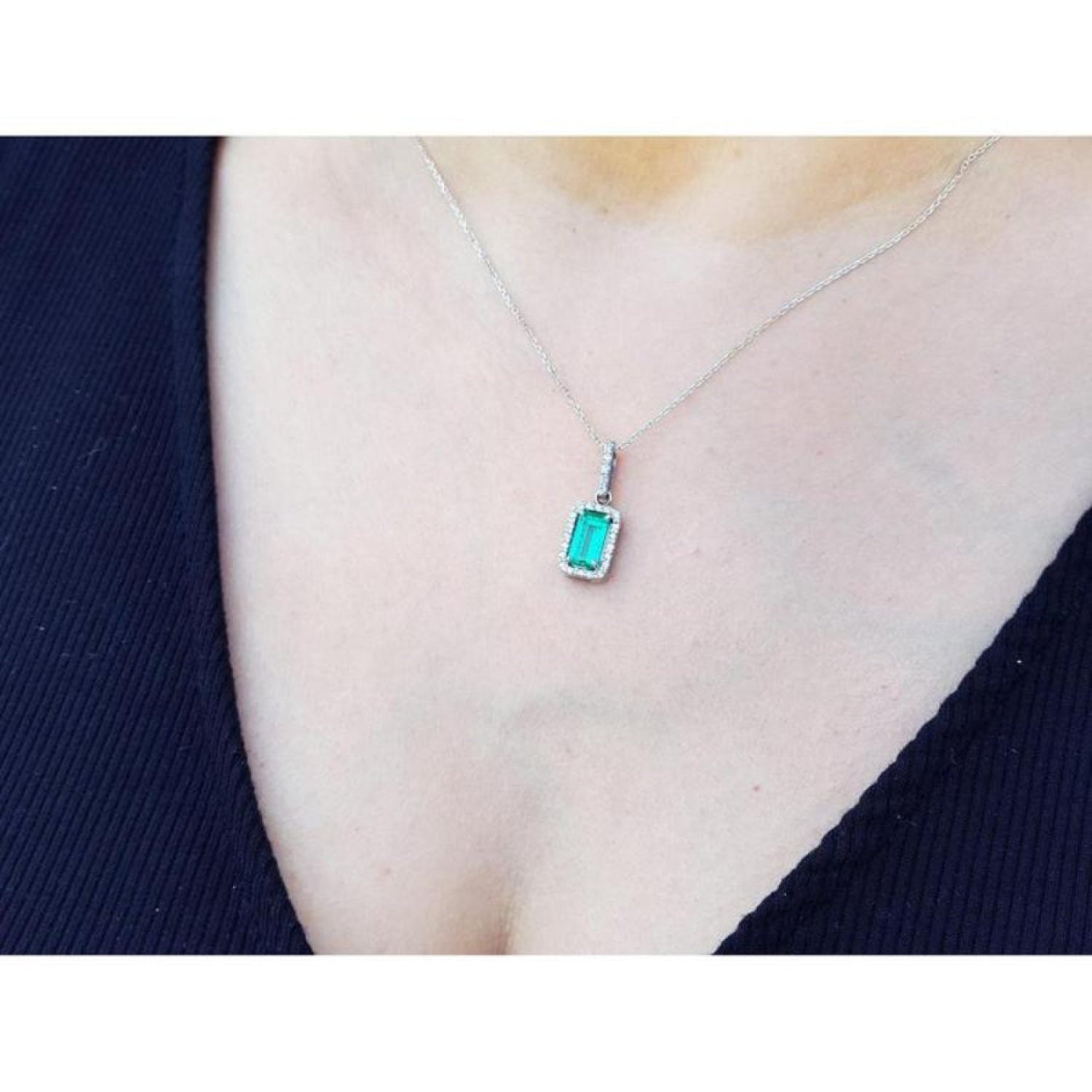 Muzo Colombian emerald pendant with diamond halo on an 18K white gold chain, worn on a person.