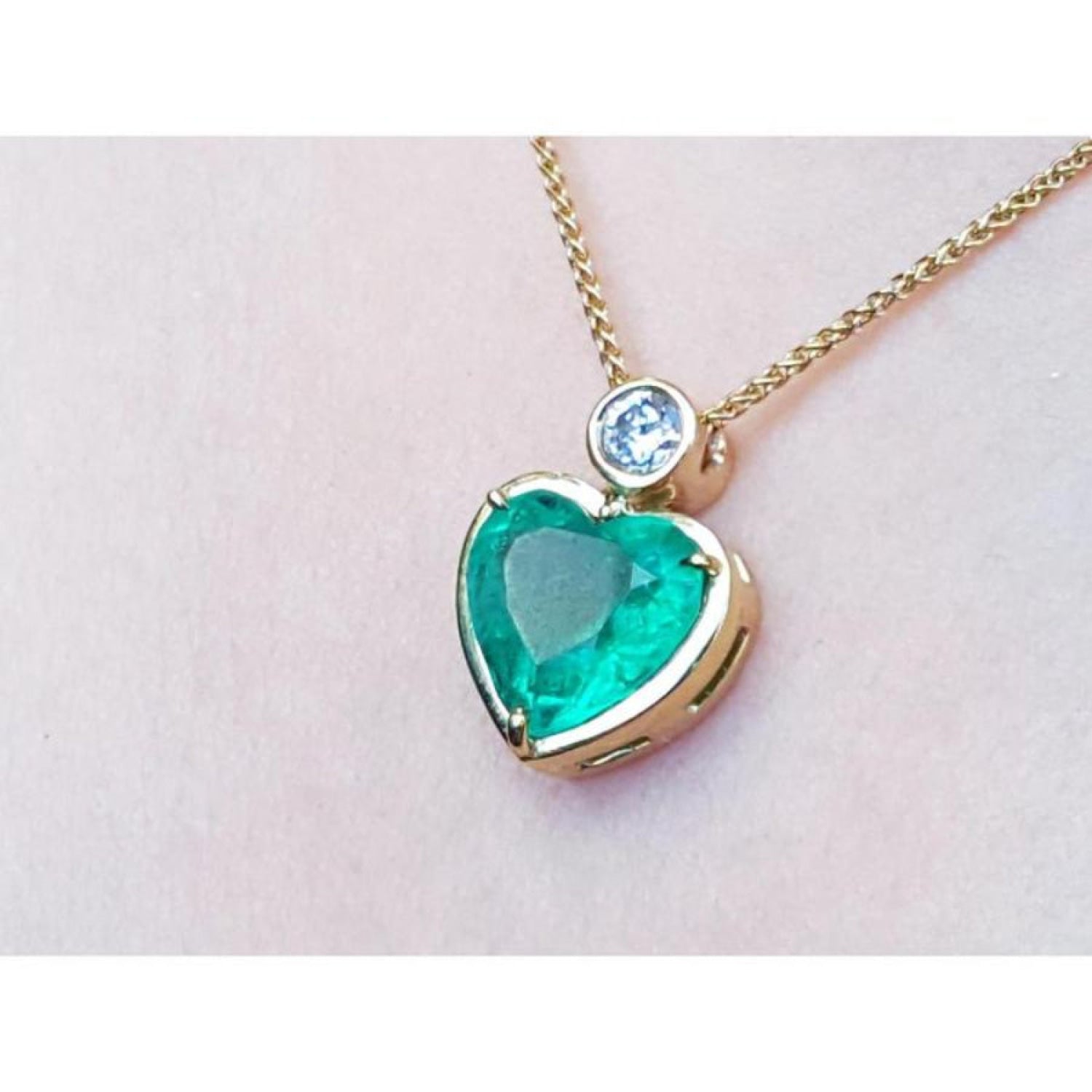 Heart-shaped emerald pendant on a 18k gold chain against a light pink skin background.