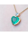 Heart-shaped emerald pendant on a 18k gold chain against a light pink skin background.