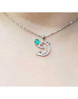 Necklace with a dolphin pendant with emerald and diamonds on a person's neck.