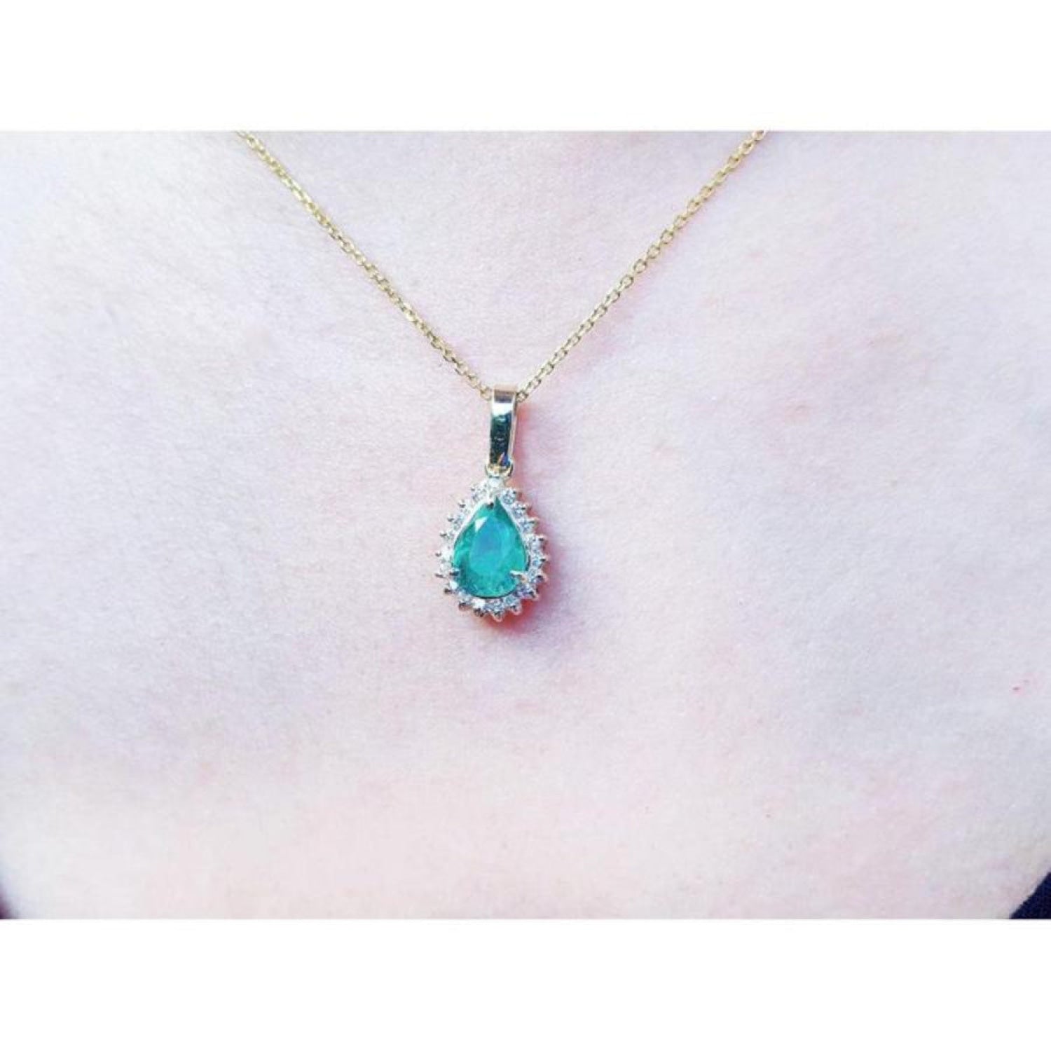 Pear-shaped Colombian emerald pendant with halo diamonds on a 14K yellow gold chain.