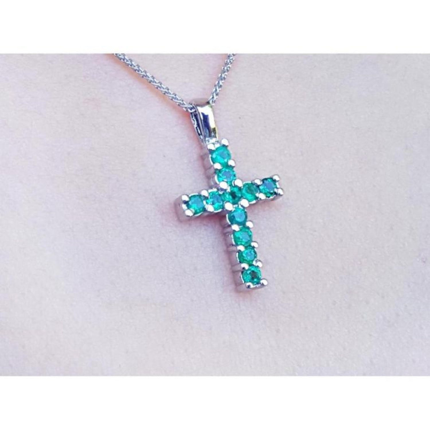 18K white gold cross pendant with round-cut emeralds on a delicate chain, worn on a person.