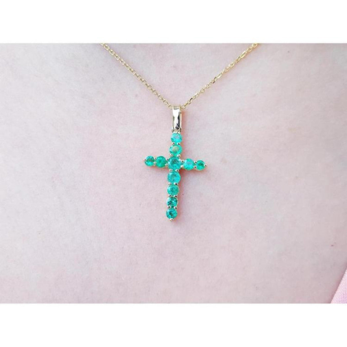 18K yellow gold cross pendant with genuine emeralds on a delicate chain, worn on a person.