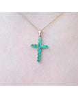18K yellow gold cross pendant with genuine emeralds on a delicate chain, worn on a person.