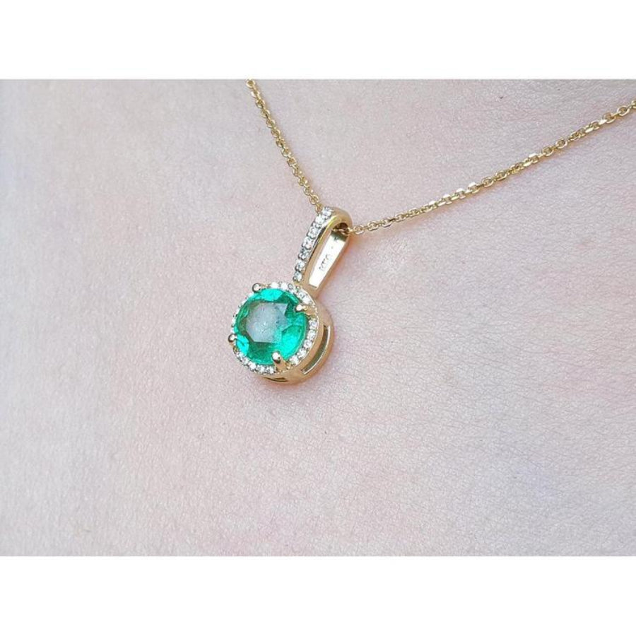 Gold necklace with a round cut natural colombian emerald pendant on a light pink skin background,