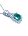 Round emerald and diamond halo pendant in 18K white gold with a deep bluish-green gemstone.