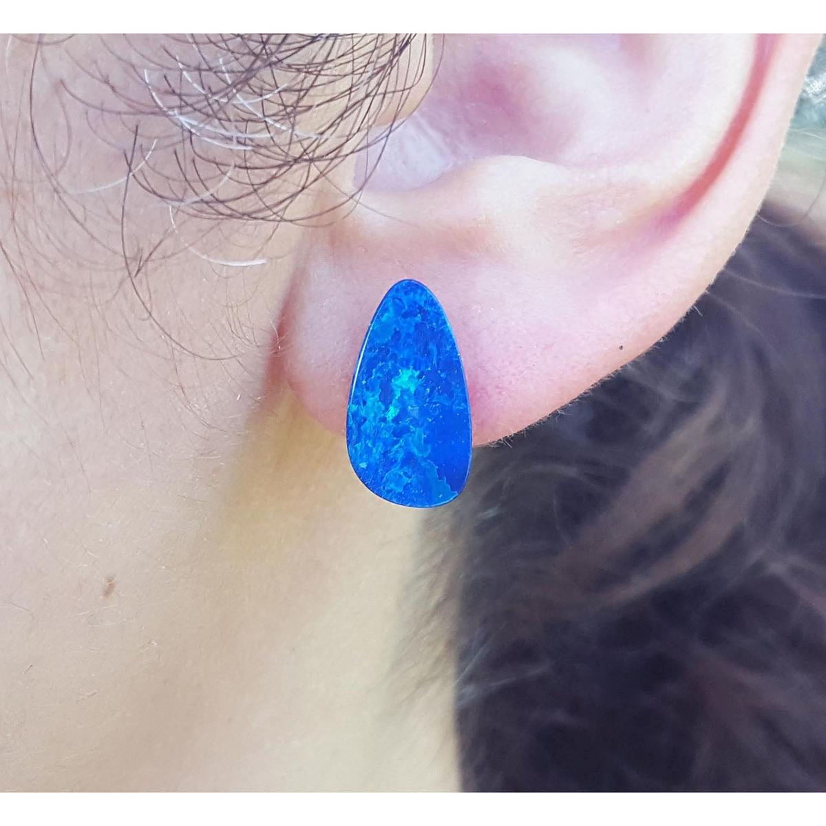 A close-up view of a doublet blue opal stud earring worn on an ear.