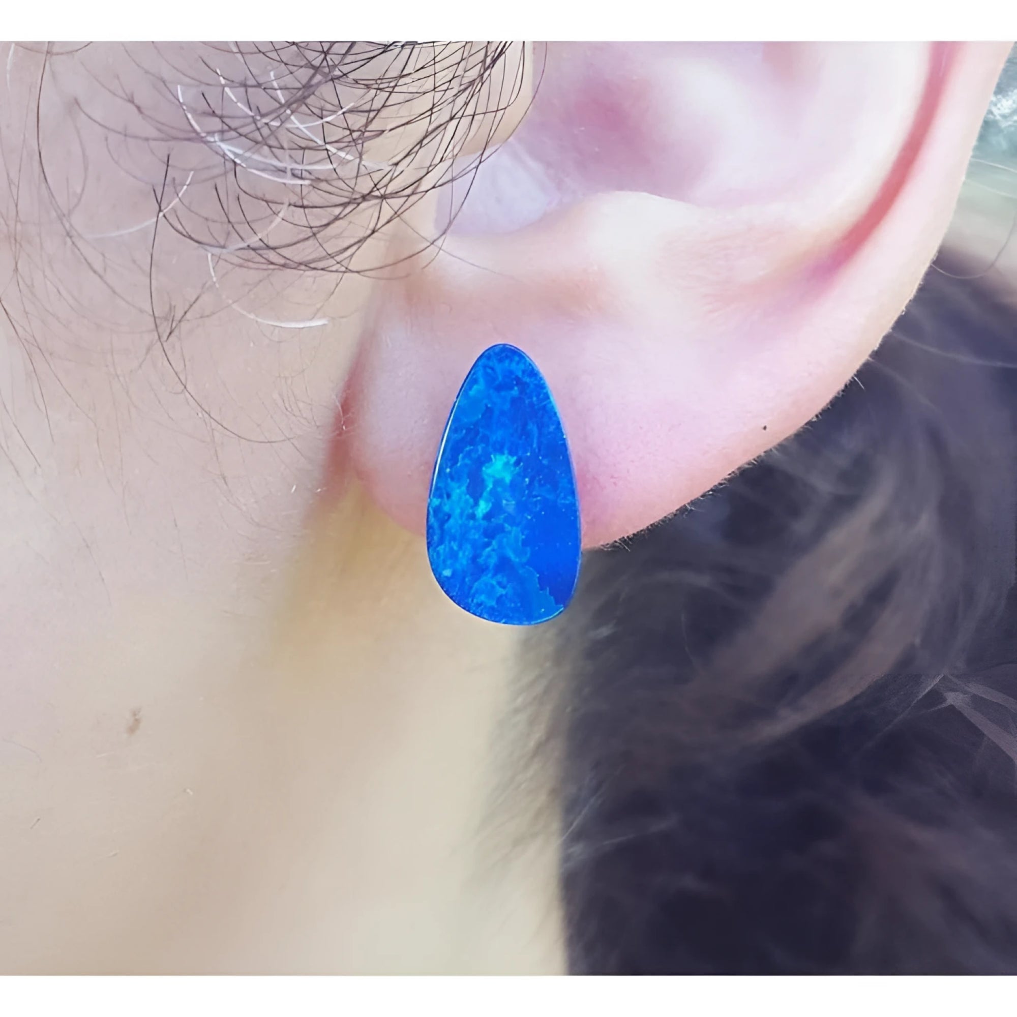 Pear-shaped Australian opal doublet earring in deep blue-green, worn on an ear.