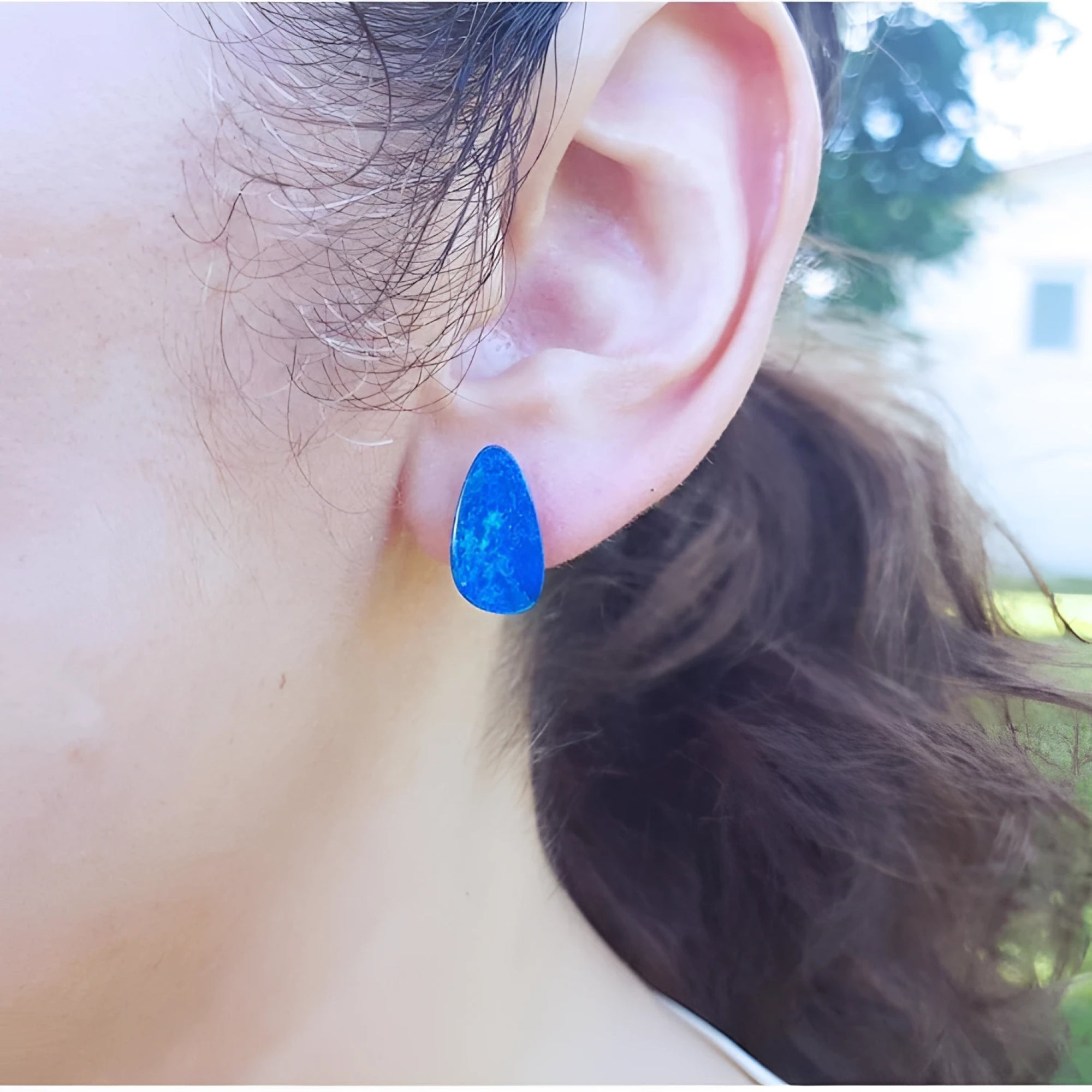 Pear-shaped Australian opal doublet earring in deep blue-green flashing colors on an ear.