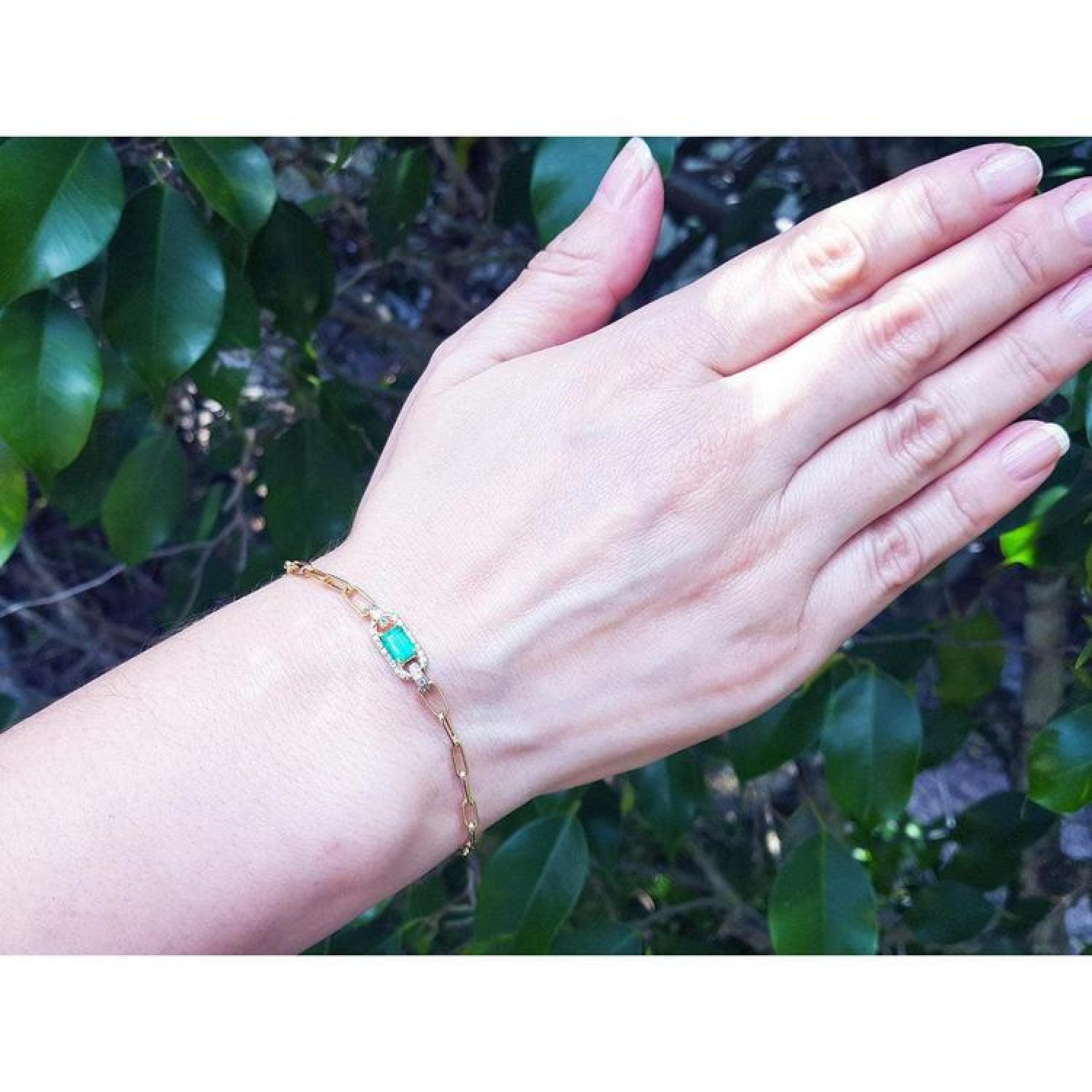 Paper clip bracelet in 14K yellow gold with a natural emerald and diamonds on a woman's wrist.