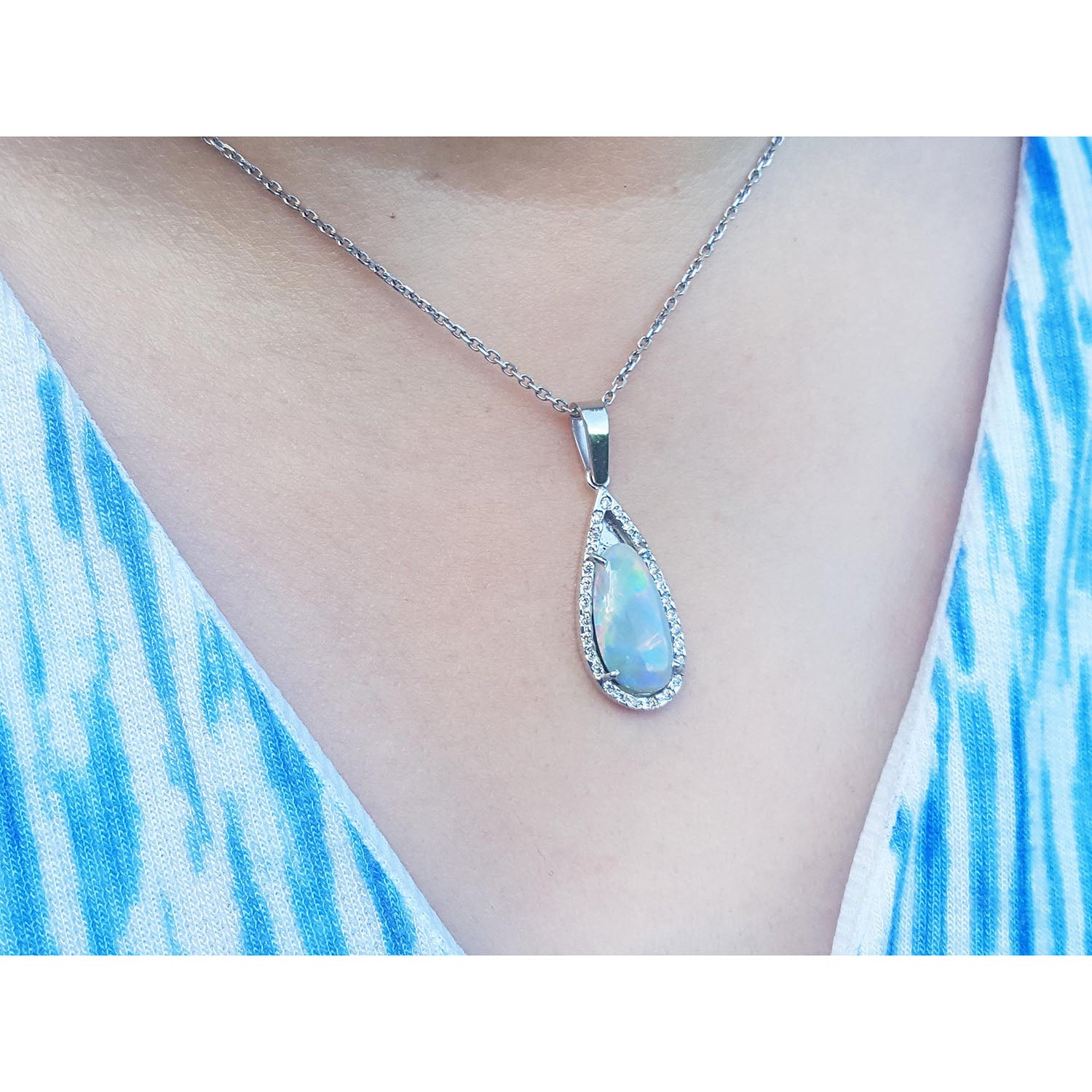 Teardrop-shaped Australian opal pendant necklace with a blue gemstone on a person wearing a blue and white patterned top.