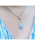 Teardrop-shaped Australian opal pendant necklace with a blue gemstone on a person wearing a blue and white patterned top.