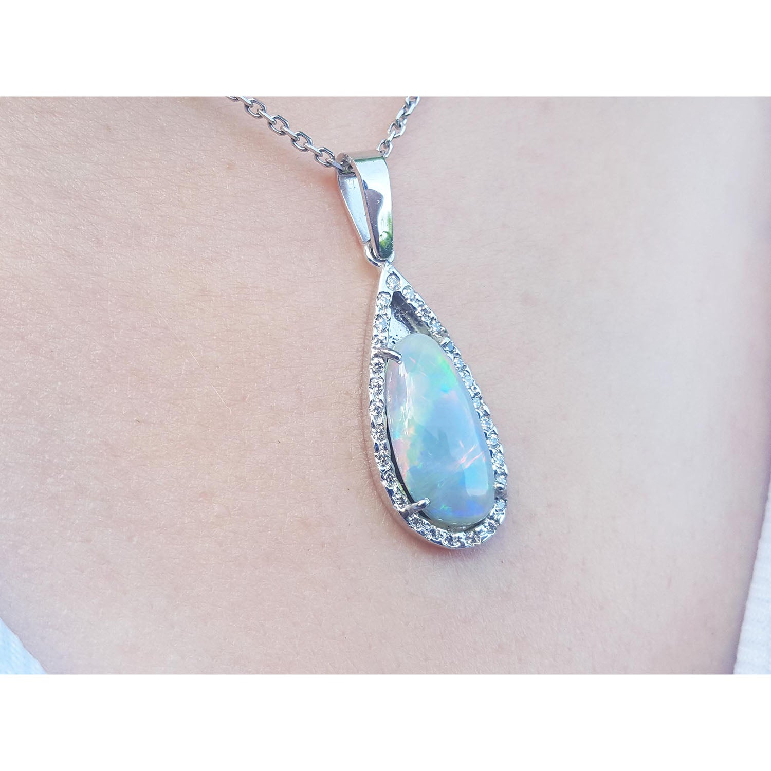 Teardrop-shaped opal pendant with diamond accents on a chain, worn on a person&#39;s neck.
