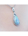 Teardrop-shaped opal pendant with diamond accents on a chain, worn on a person's neck.