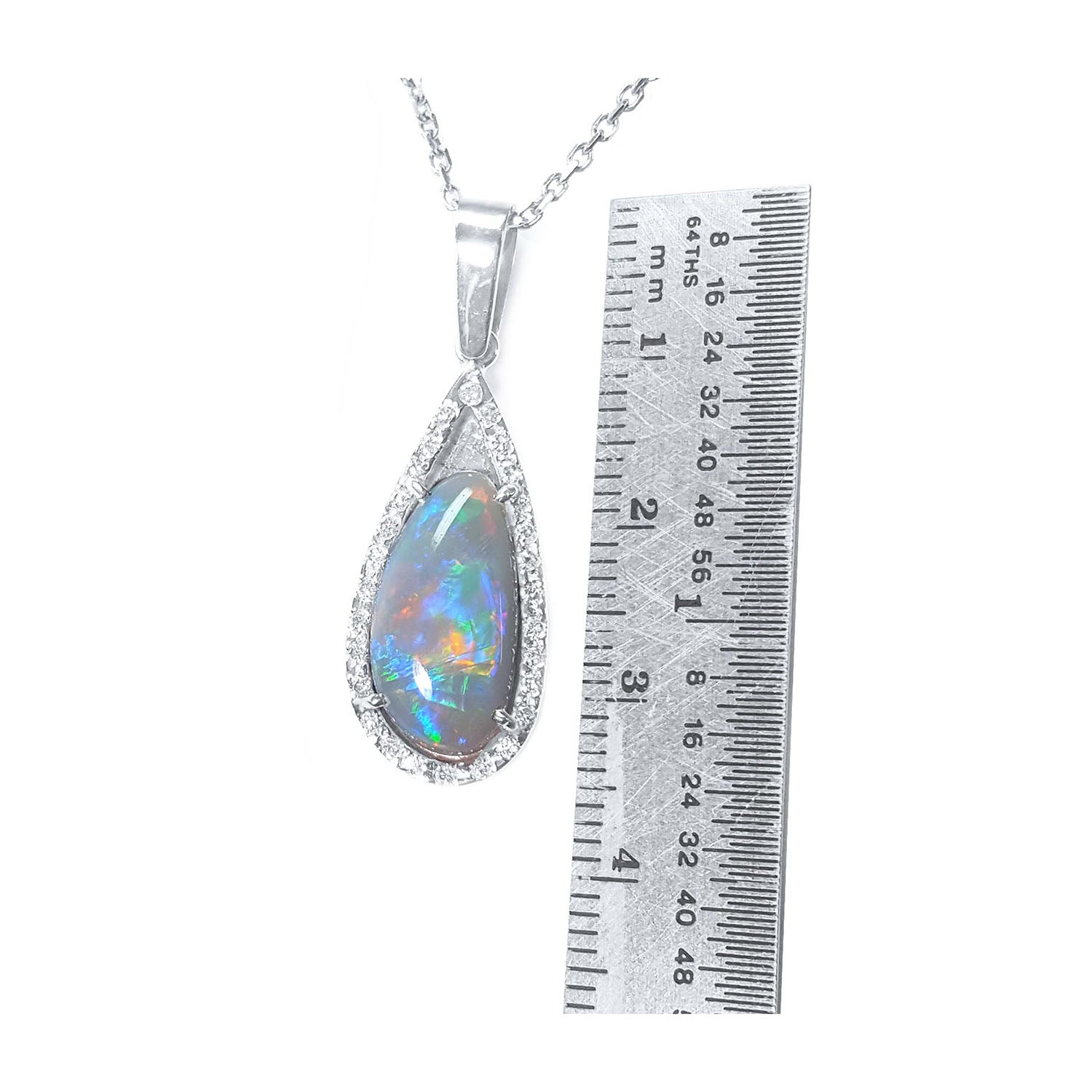 Teardrop-shaped opal pendant on a white gold chain with a ruler for scale on a white background.