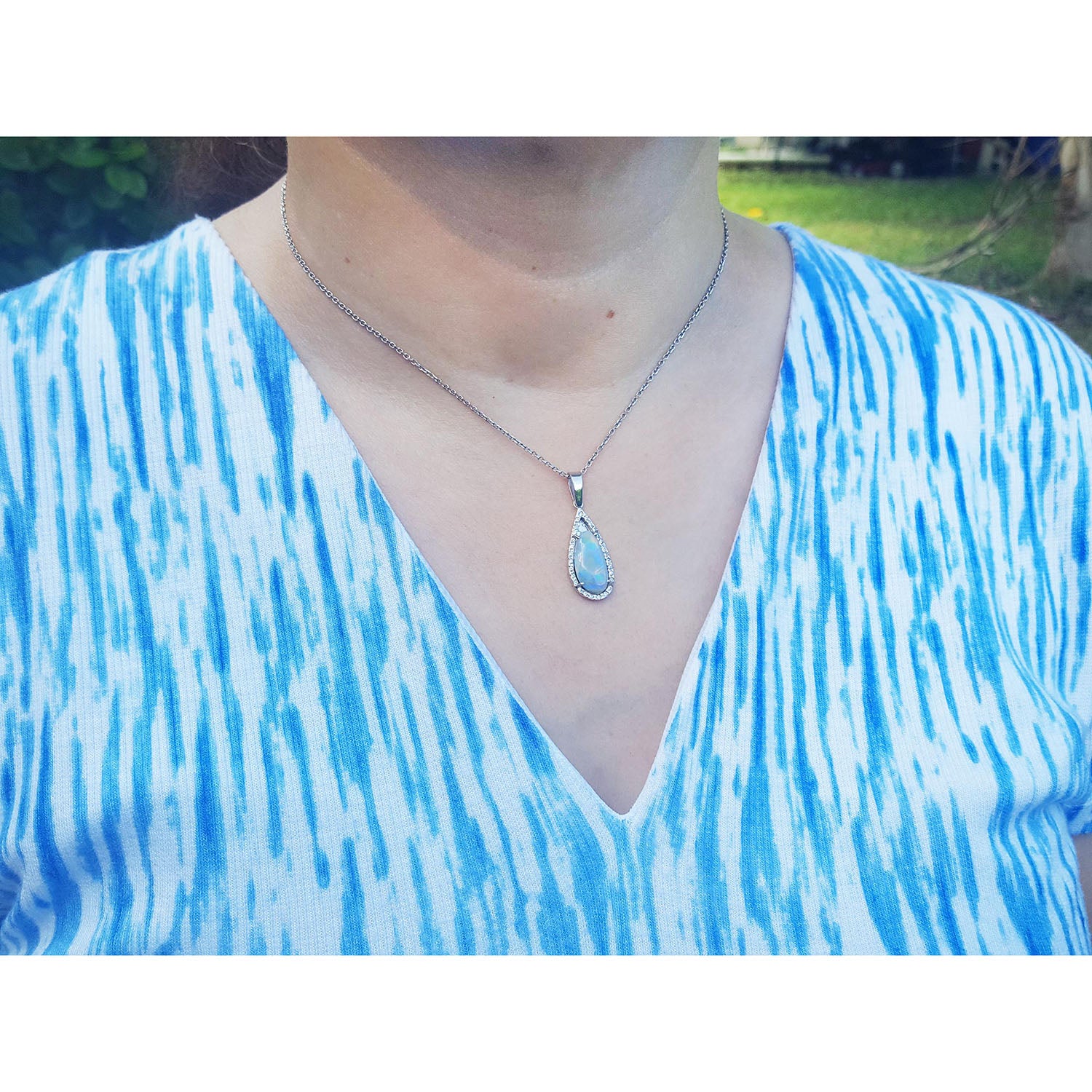 A lady wearing a blue and white patterned top with a necklace featuring a teardrop-shaped opal pendant.