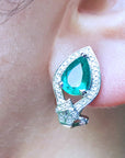 Teardrop-shaped emerald green gemstone earring worn on an ear.
