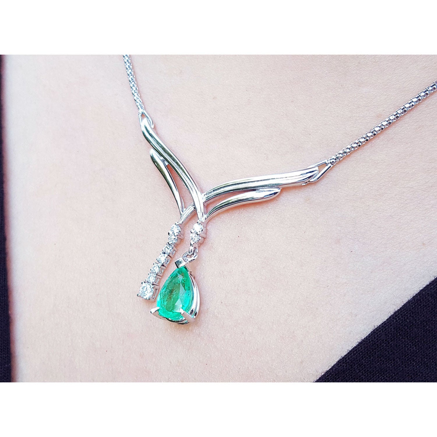 14K white gold necklace with a pear-shaped emerald pendant and diamond accents on a chevron design.