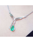14K white gold necklace with a pear-shaped emerald pendant and diamond accents on a chevron design.