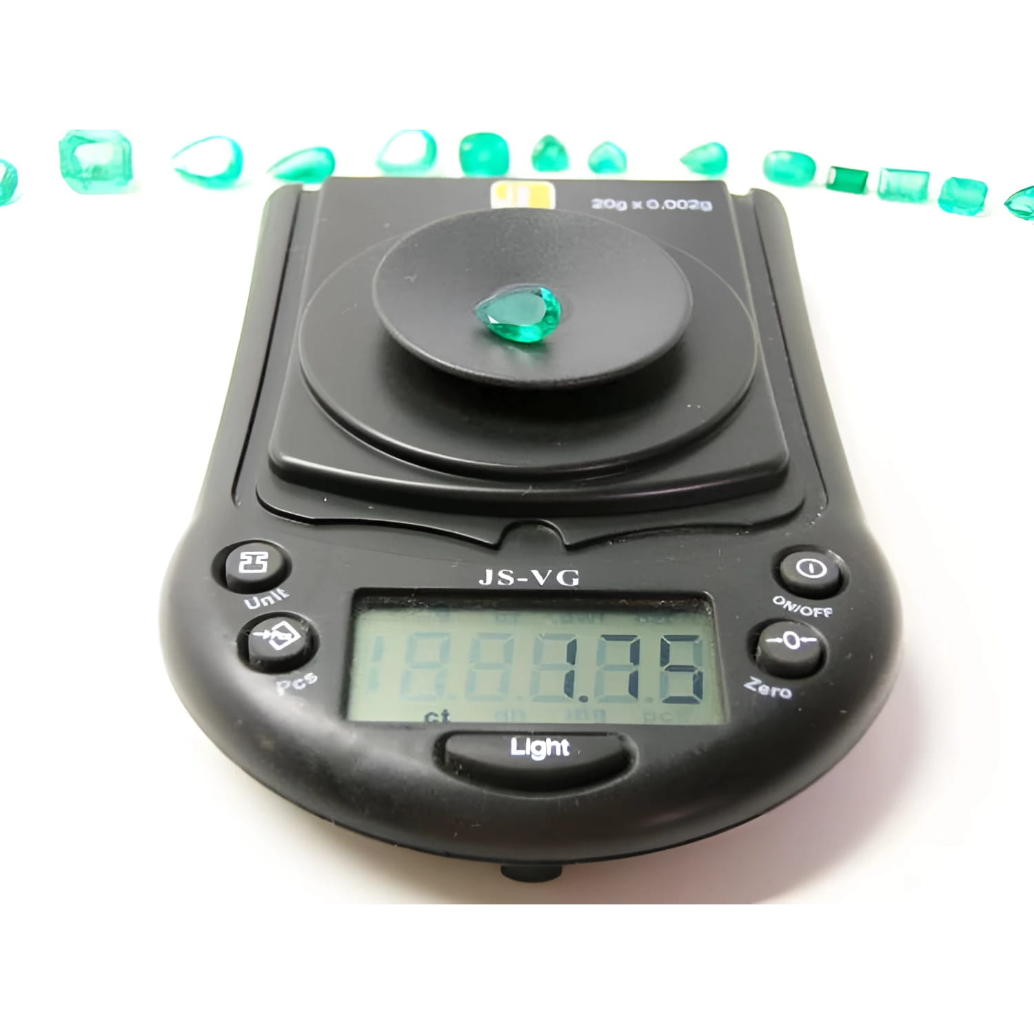 1.74-carat pear-cut Colombian emerald on a digital scale, with other emeralds in the background.