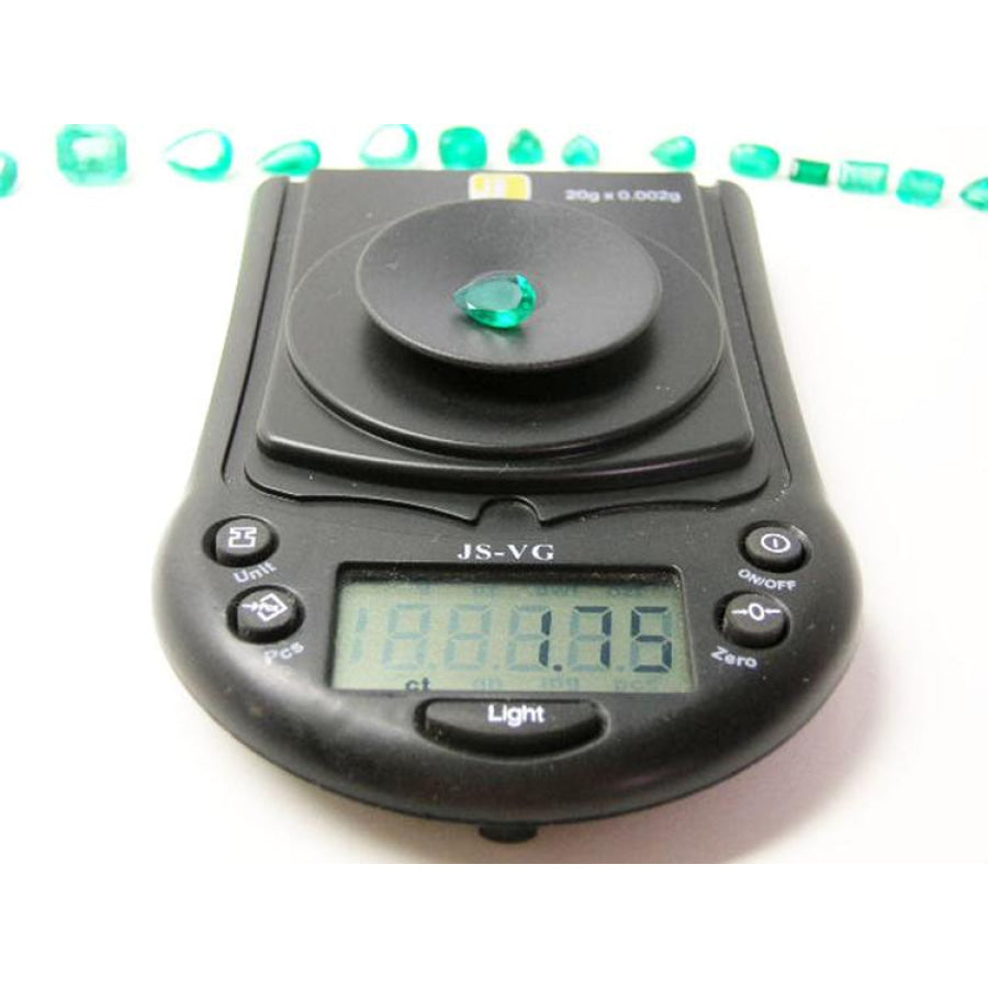 1.74-carat pear-cut Colombian emerald on a digital scale, with other emeralds in the background.