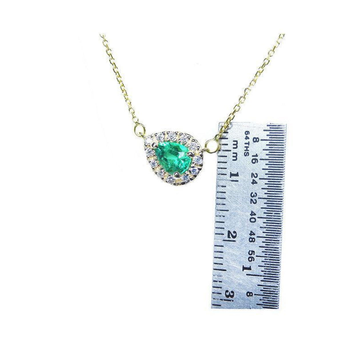 Emerald pear-shaped necklace with diamond halo on 14K yellow gold chain, next to a ruler for scale.