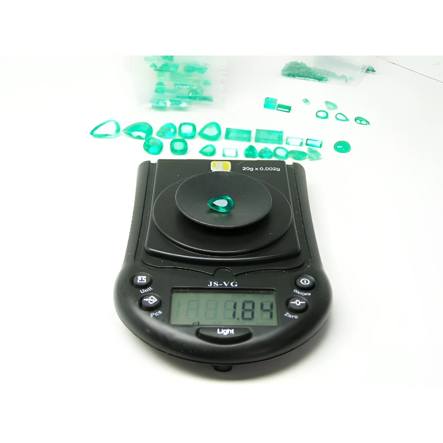 1.84 carat pear-cut natural Muzo Colombian emerald on a digital scale, surrounded by other green emeralds.
