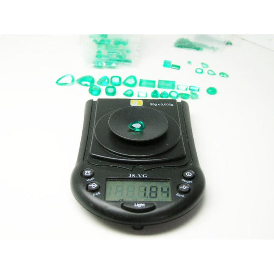 1.84 carat pear-cut natural Muzo Colombian emerald on a digital scale, surrounded by other green emeralds.