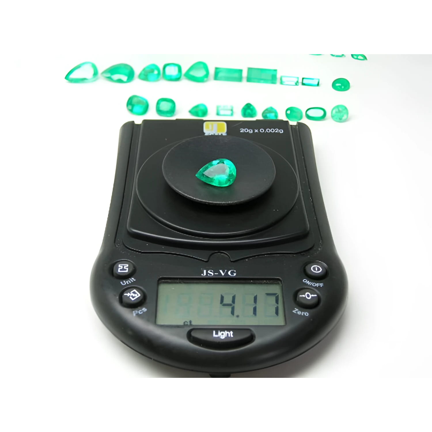 4.17 ct pear-cut natural Muzo Colombian emerald on a digital scale, with other emeralds in the background.