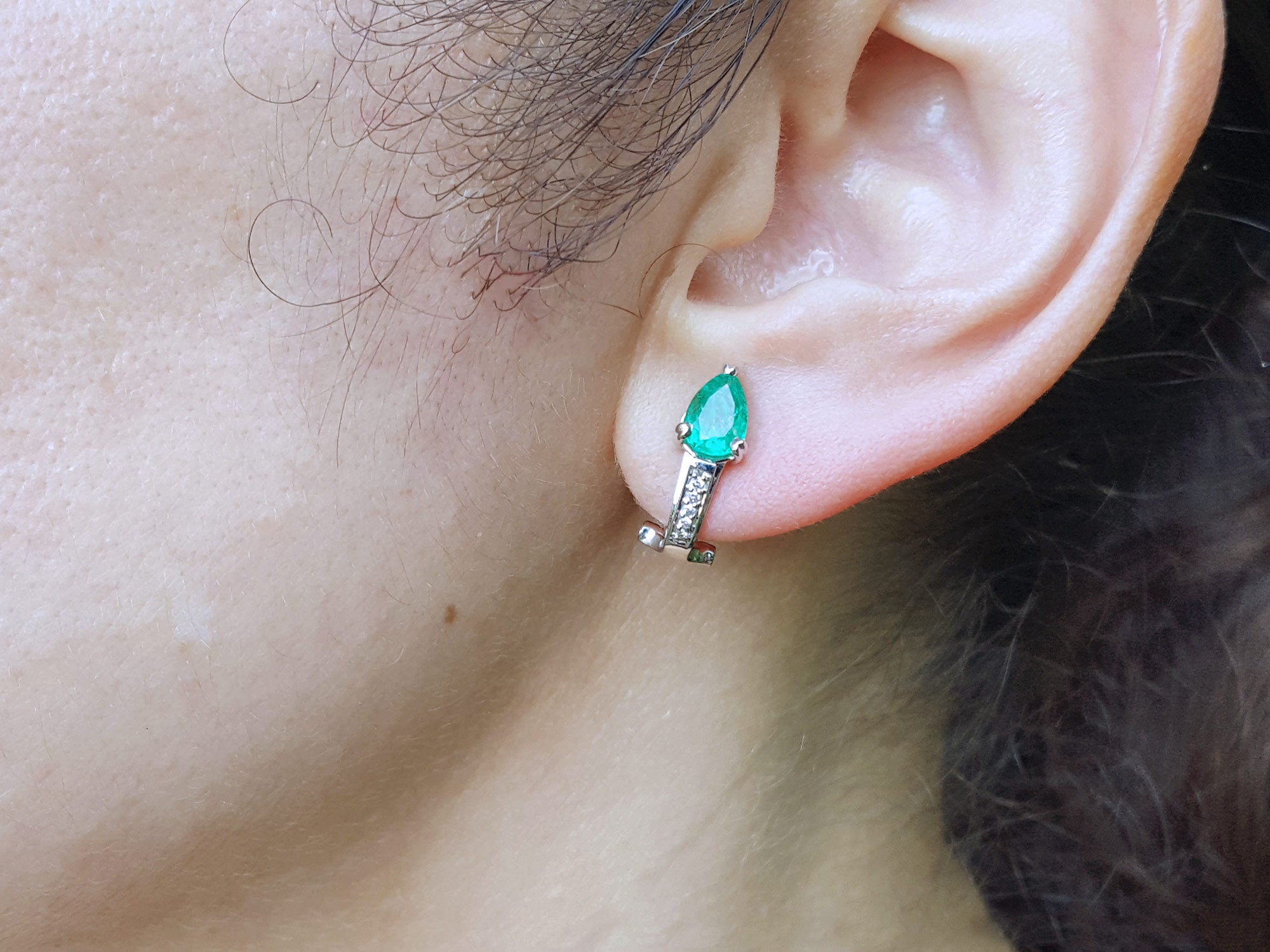 Close-up of an woman&#39;s ear wearing a pear cut emerald earring.