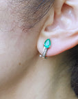 Close-up of an woman's ear wearing a pear cut emerald earring.