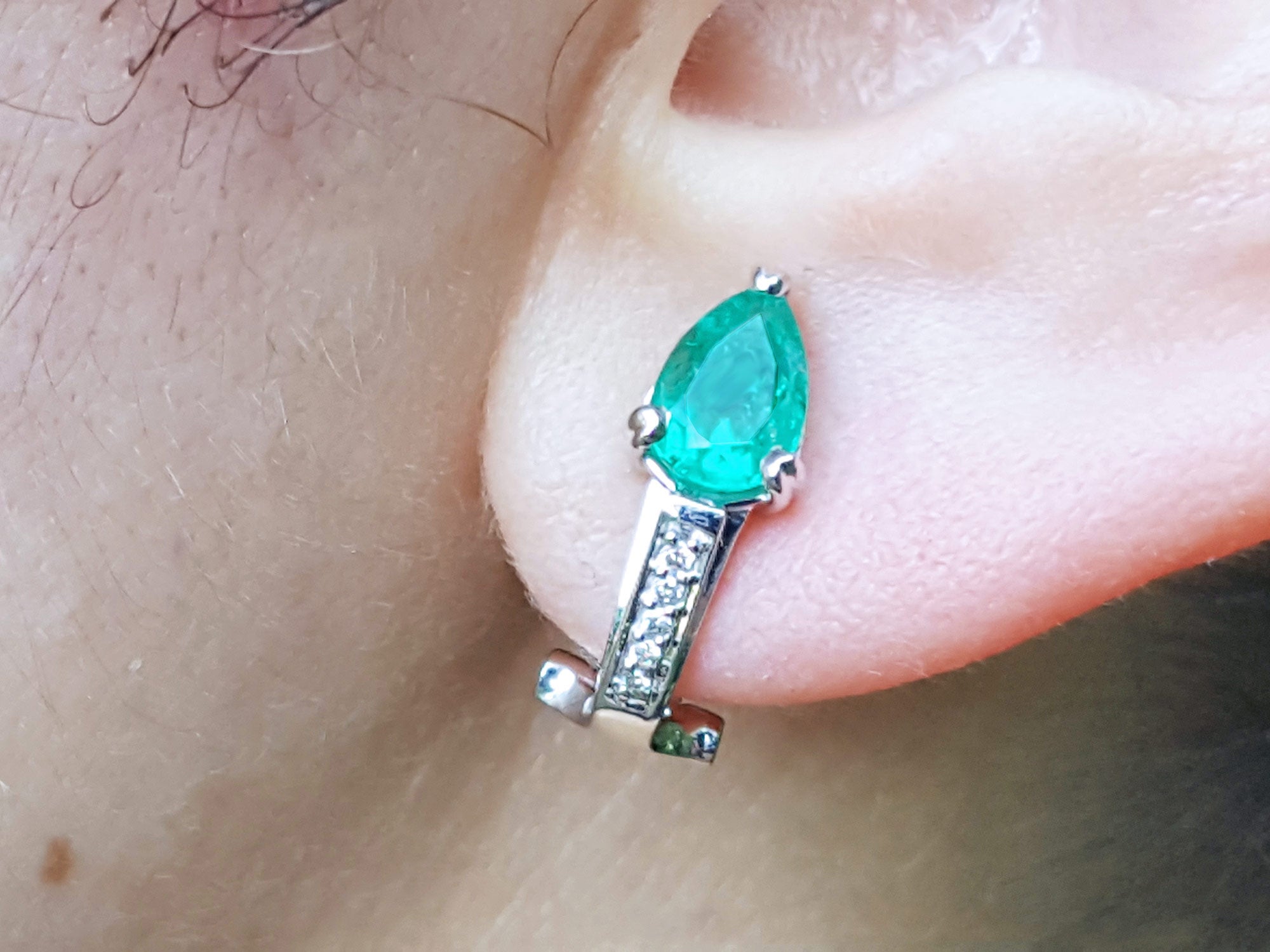 Close-up of a teardrop emerald earring on an ear. gift for Mother&#39;s Day