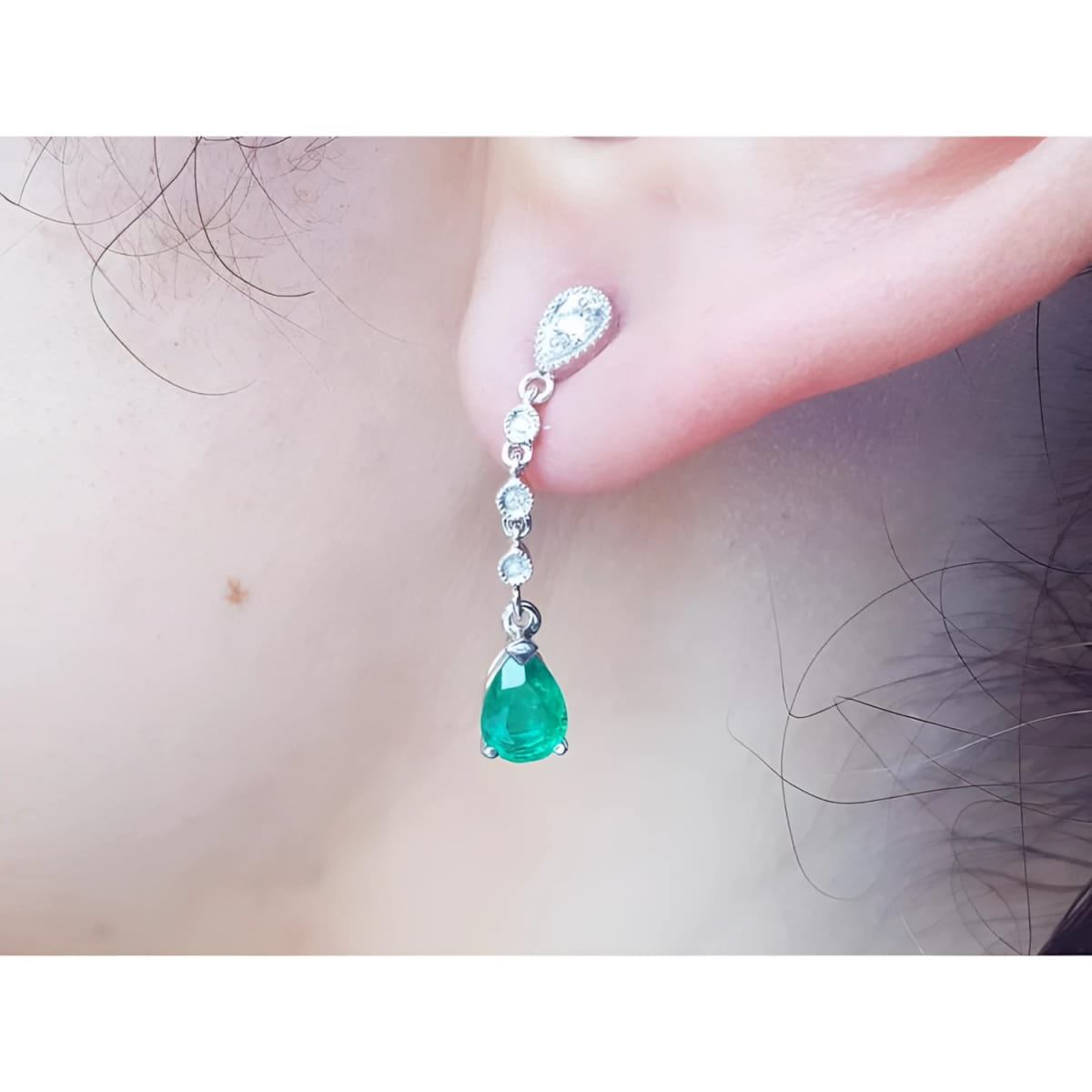 Close-up of a natural colombian  emerald teardrop earring in white gold on a person's ear.