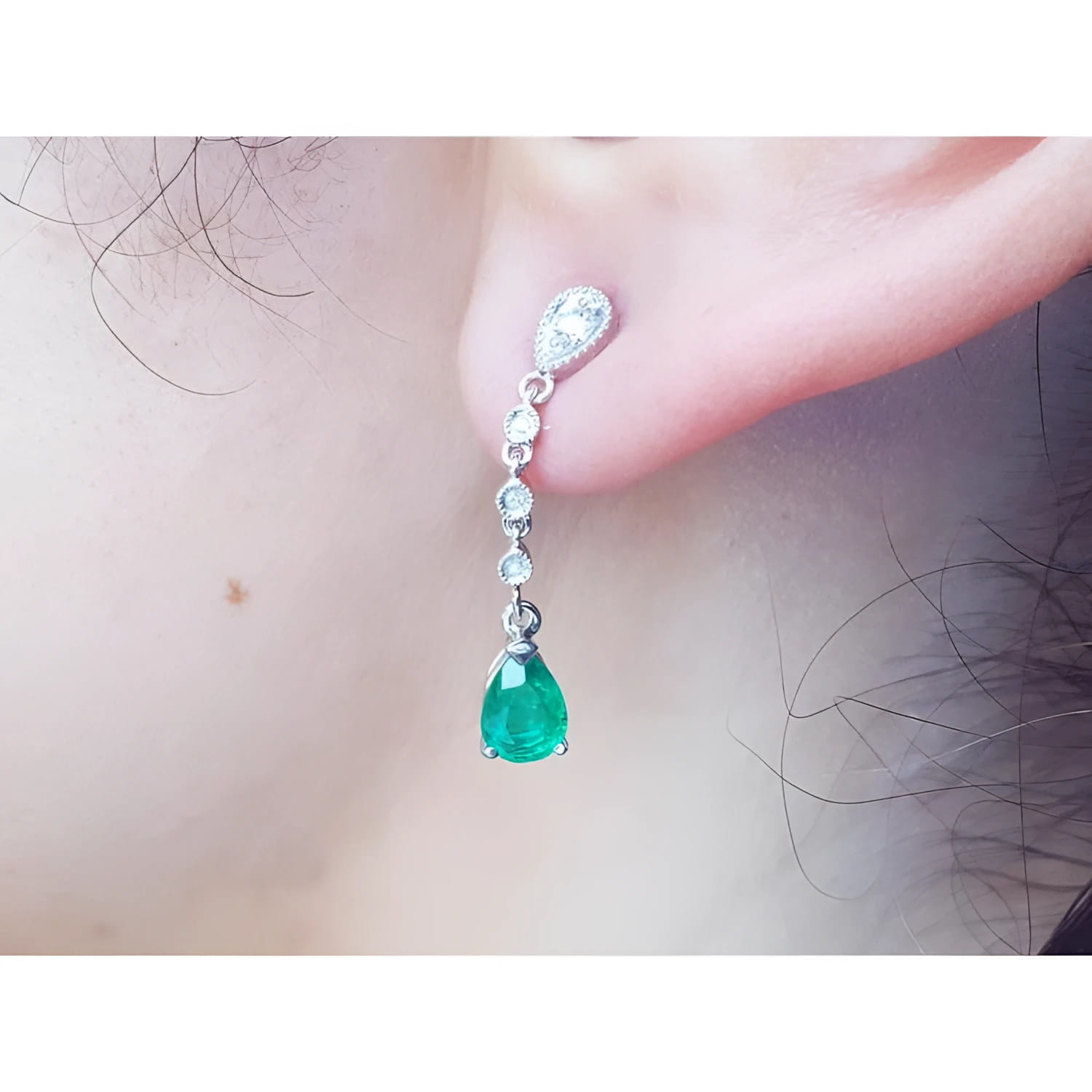 Close-up of a natural colombian  emerald teardrop earring in white gold on a person's ear.