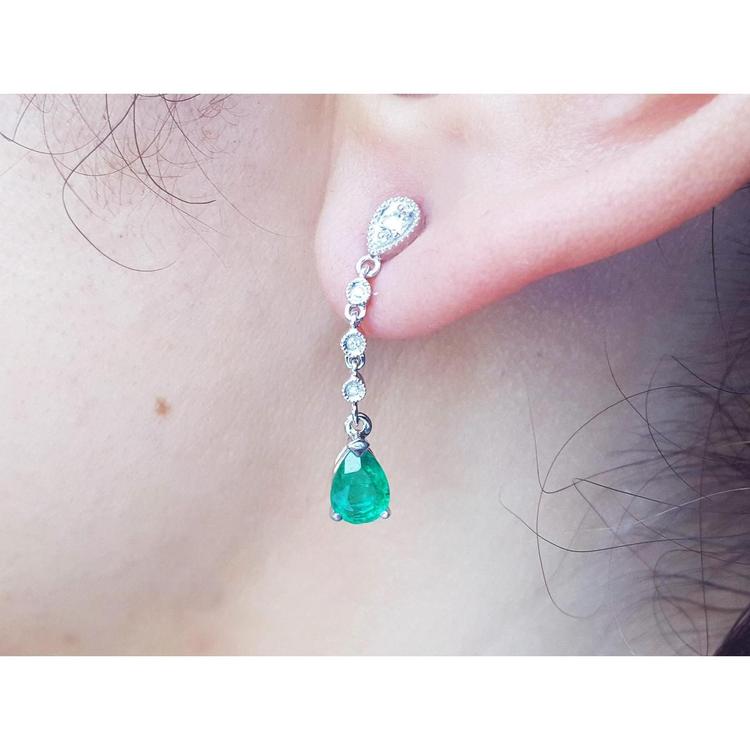 Close-up of a natural colombian  emerald teardrop earring in white gold on a person's ear.