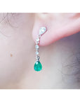 Close-up of a natural colombian  emerald teardrop earring in white gold on a person's ear.