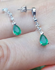 Genuine teardrop emerald earrings with diamond accents on a hand.