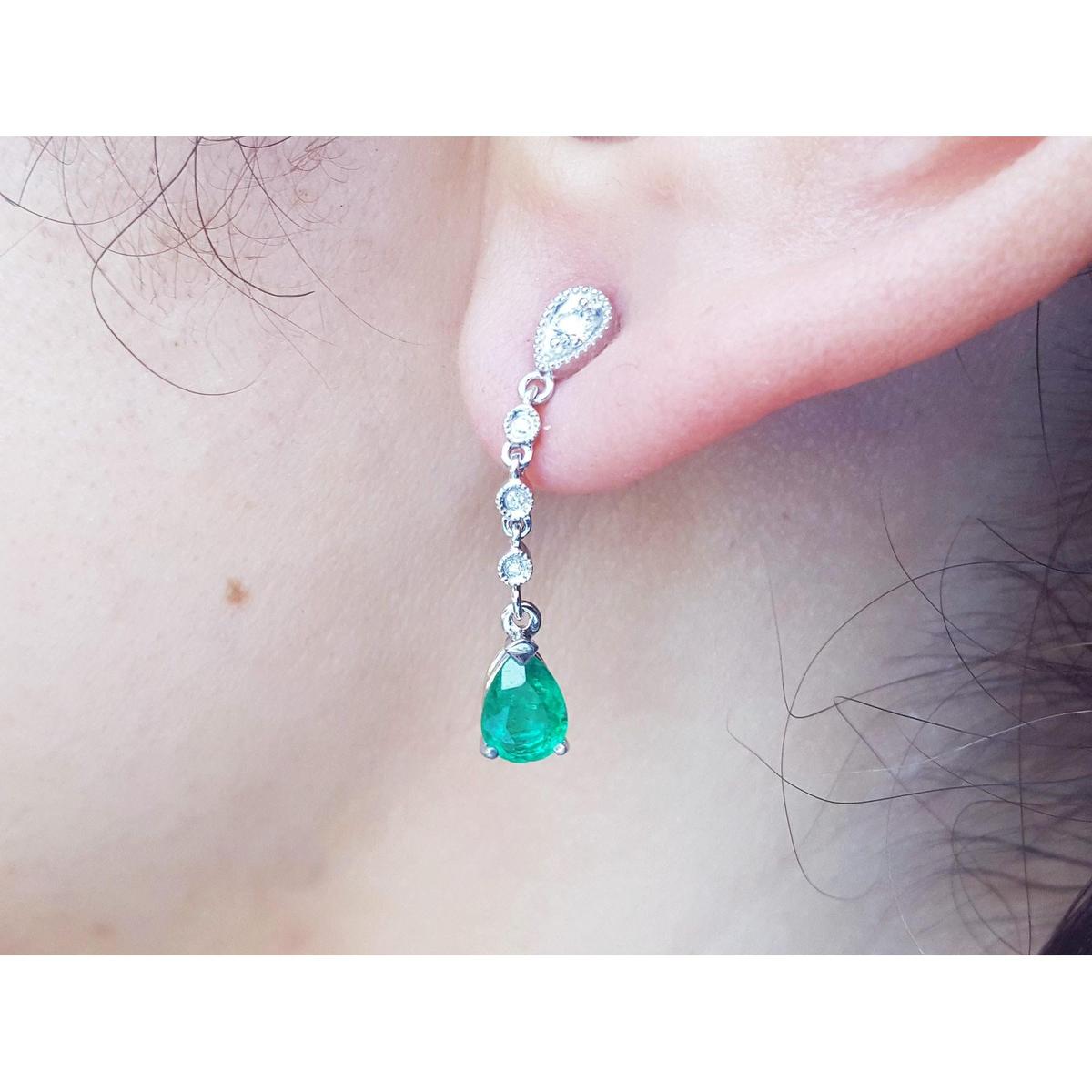 Close-up of an emerald teardrop earring on a person's ear.