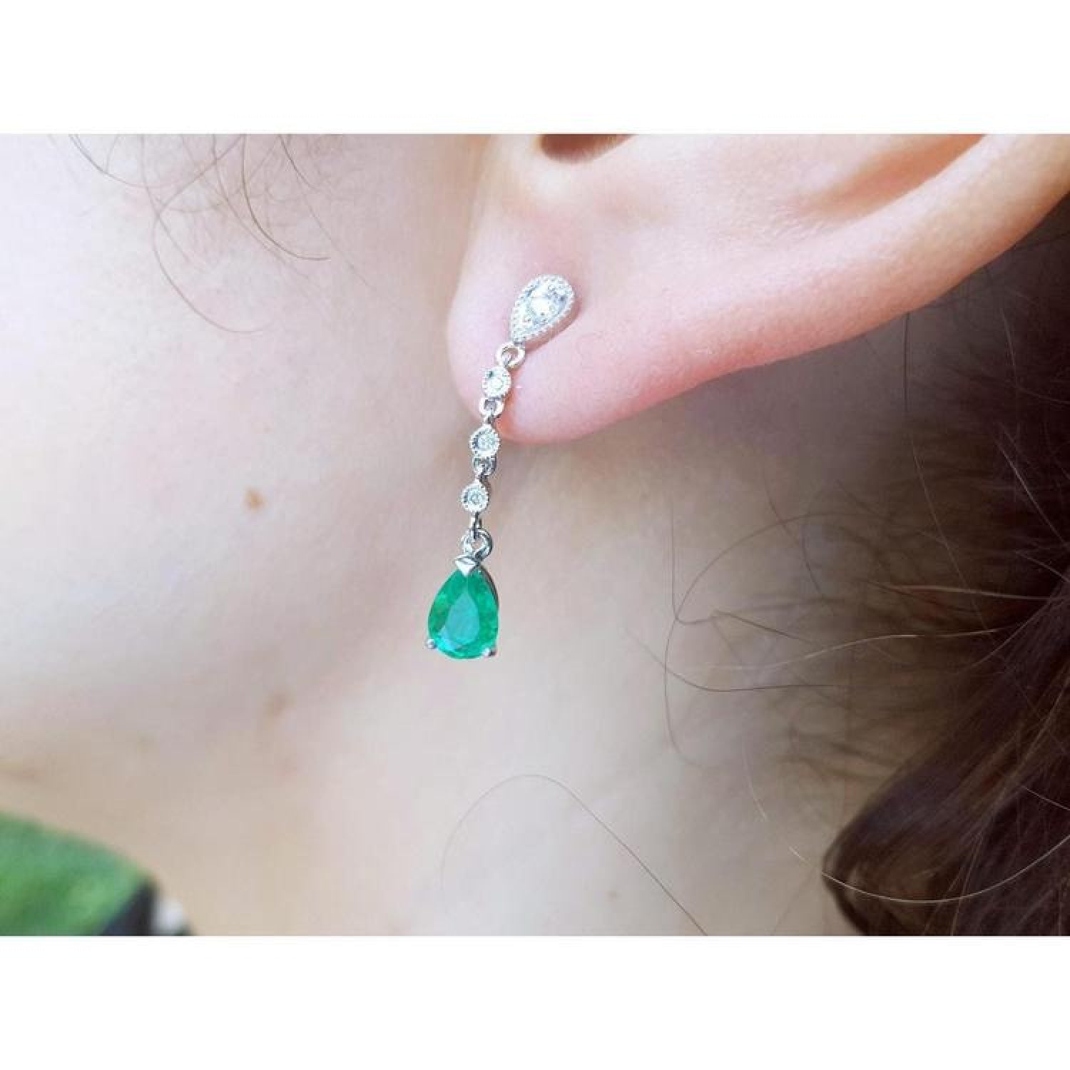 14K white gold pear-shaped emerald drop earring with brilliant white diamonds on an ear.