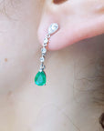Close-up of a woman wearing an emerald teardrop earring with accent diamonds.
