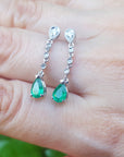 Natural teardrop emerald earrings with diamond accent on a hand.